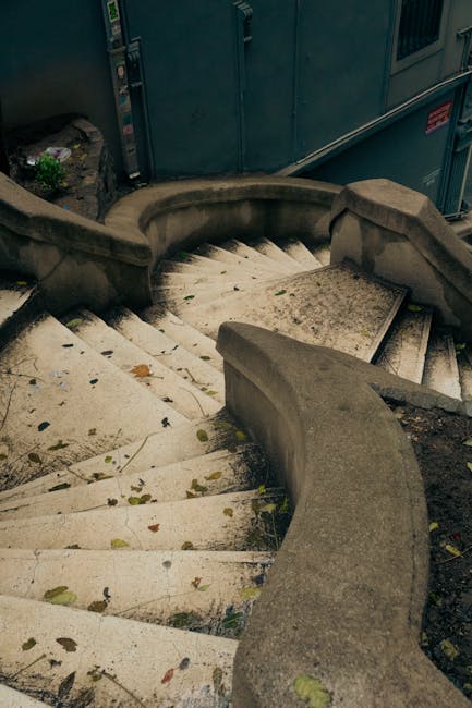 Inside a residential property during a home relocation, a staircase with red patterned carpet leads down to a lower level where a partly dismantled doorway reveals a dark hole or hatch, possibly for m